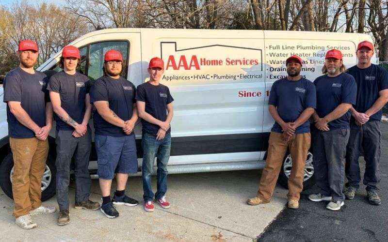 Seven people in red caps pose beside an AAA Home Services van in a driveway.