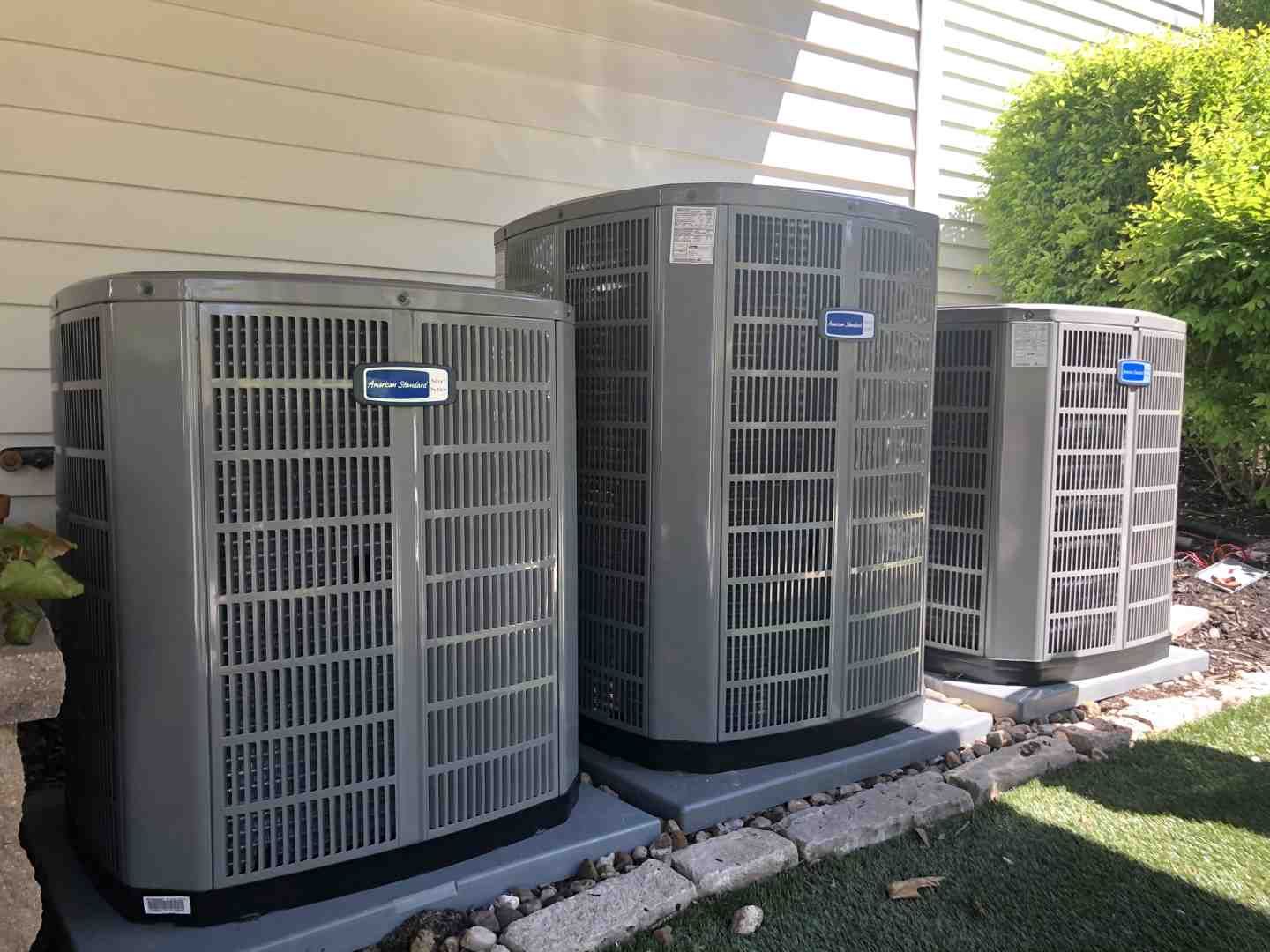 Three outdoor HVAC units beside a house on a gravel bed