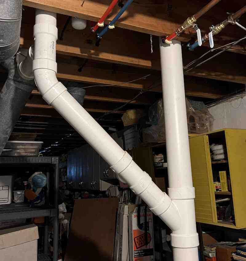 White plumbing ducts and pipes running across an unfinished basement ceiling.