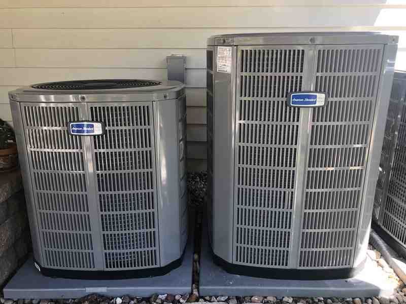 Two outdoor air conditioning units beside a house wall, one round and one rectangular.