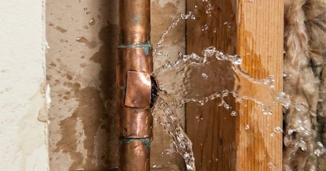 Leaking copper pipe spraying water inside a wall cavity near wood framing and drywall