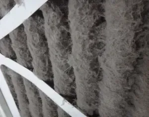 Close-up of a dusty air filter with gray lint and white crossbars