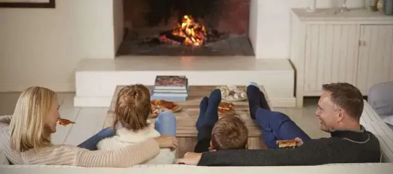 People relaxing on a couch facing a lit fireplace in a cozy living room