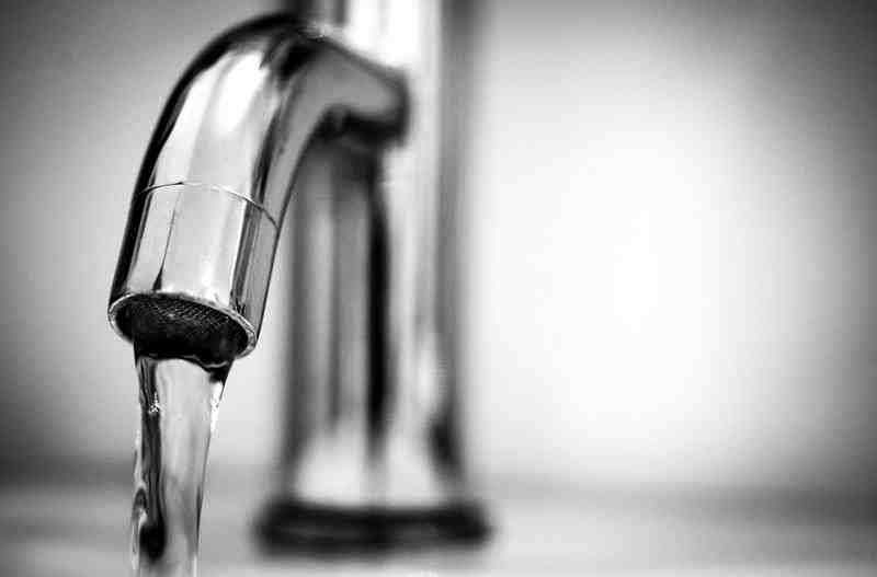 Close-up of a chrome faucet dripping water over a sink, in black and white.