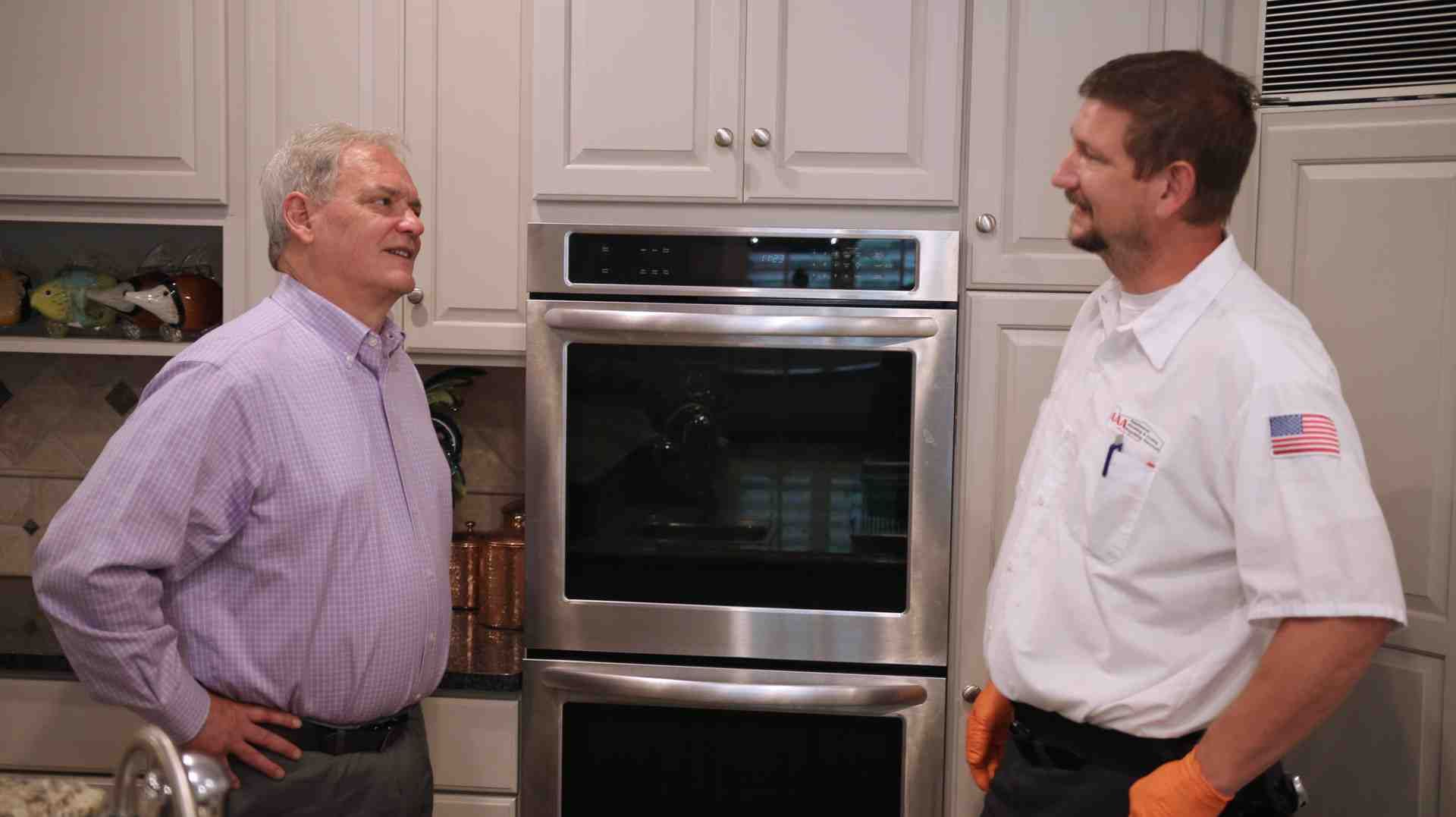Two men talking in a kitchen beside a stainless steel double oven.