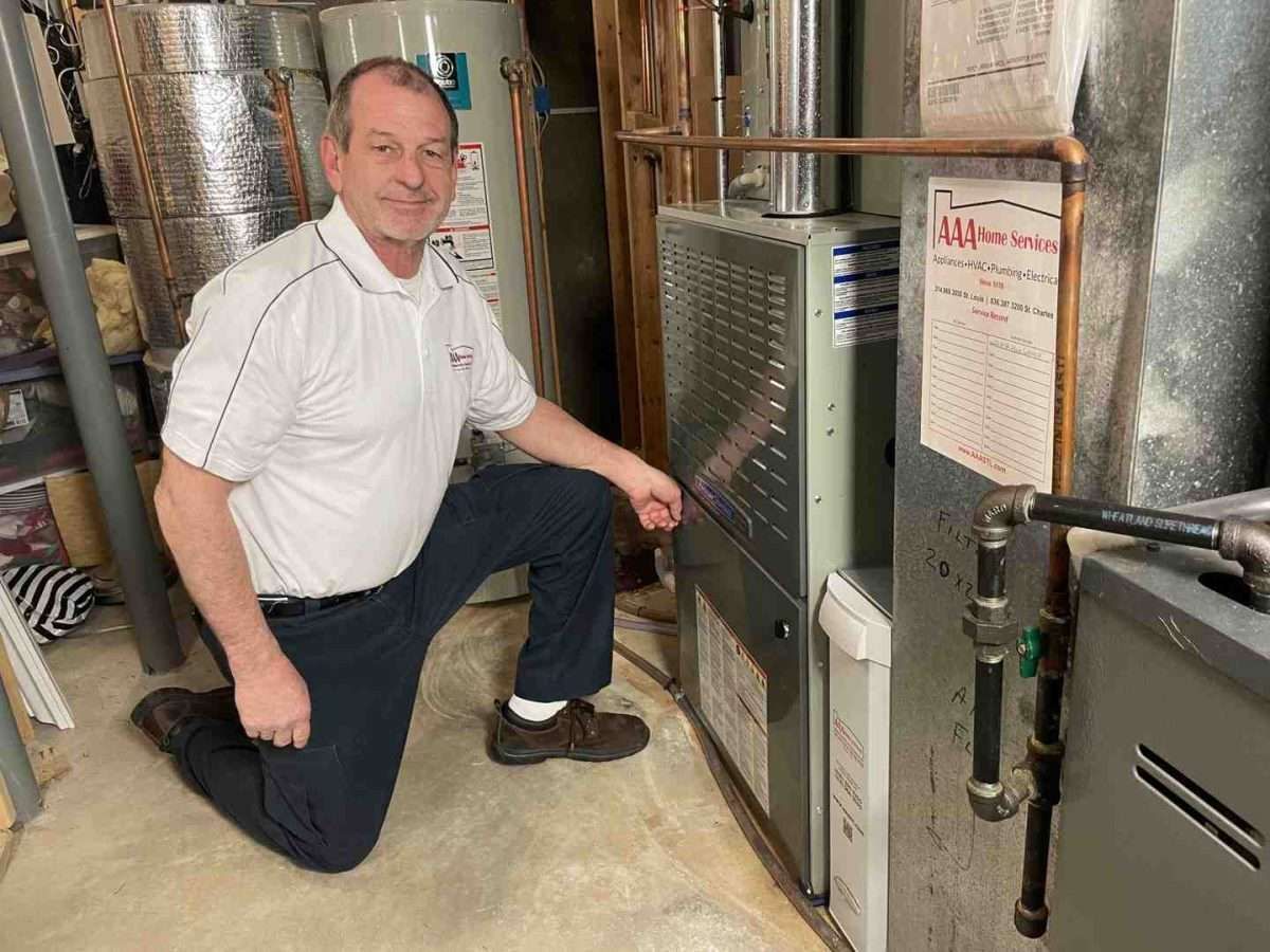 Technician kneeling beside a furnace in a utility room, inspecting ductwork and equipment.