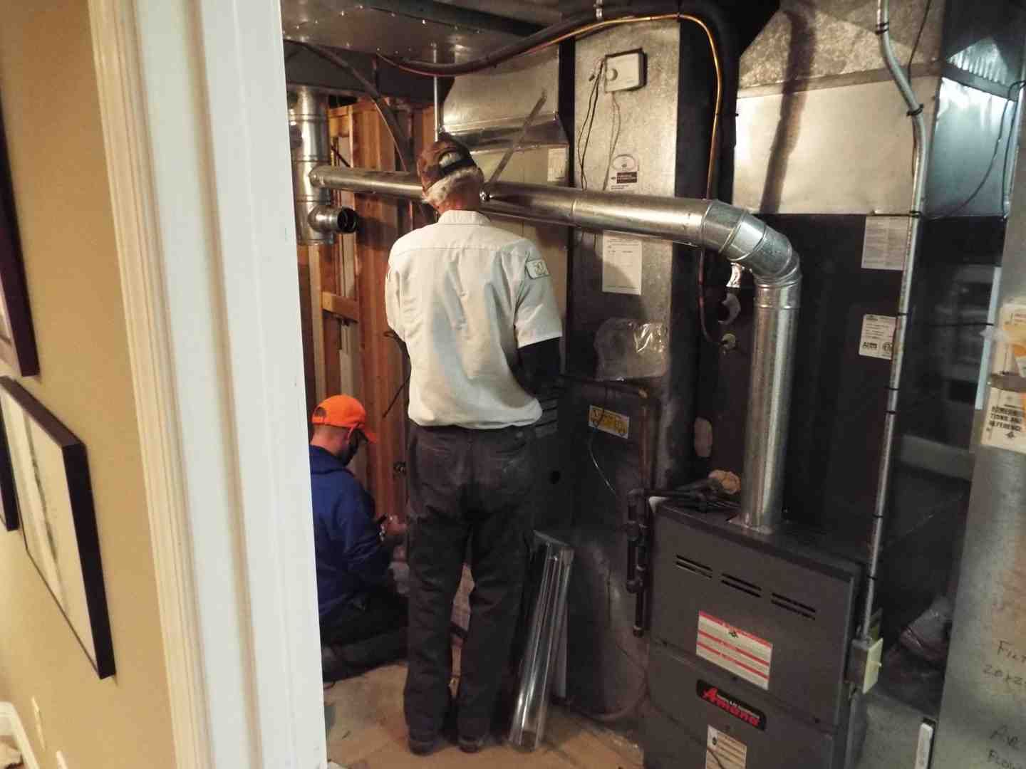 Technicians inspecting a furnace and ductwork in a basement utility room