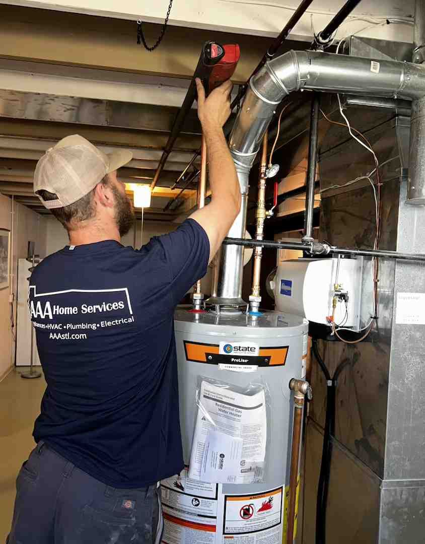 Technician using a red drill to install ductwork above a water heater in a basement utility room