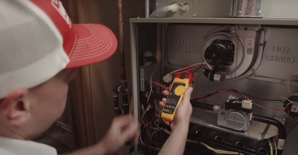 Technician testing wiring inside an open electrical panel with a multimeter and flashlight
