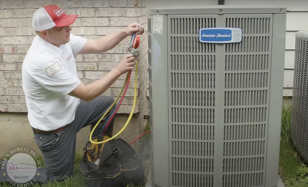 Technician using gauges to service an outdoor air conditioning unit beside a house