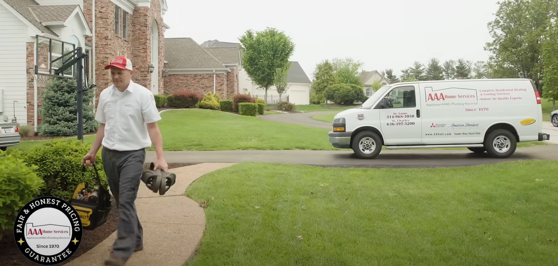 Man in red cap walks on a suburban sidewalk beside a white service van near a brick house.