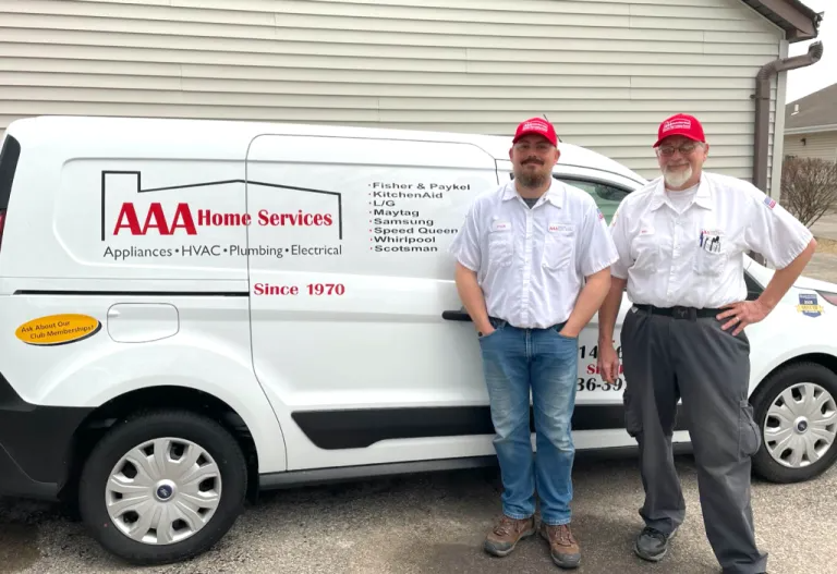 Two AAA Home Services workers in white shirts and red caps standing beside a service van