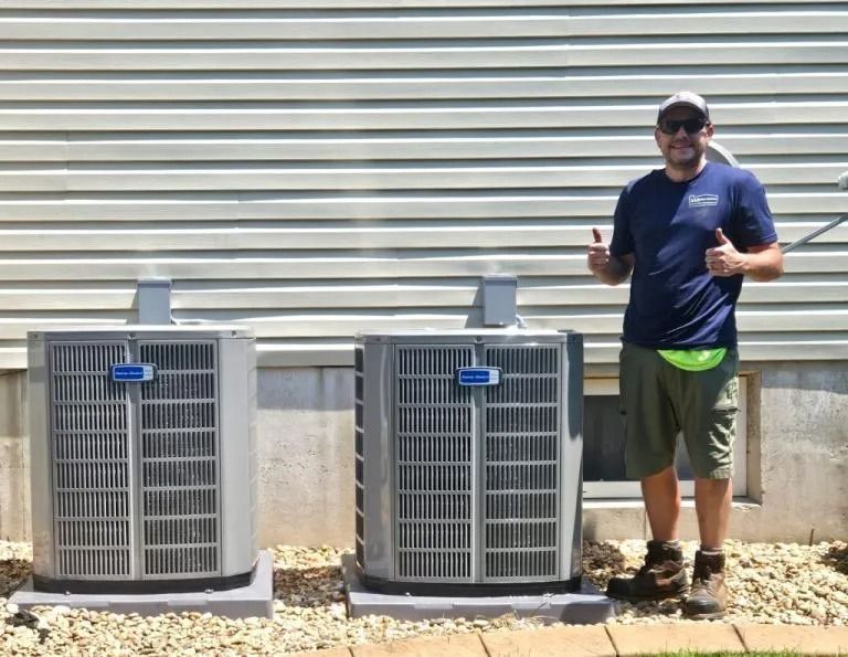Man standing by two outdoor HVAC units beside a building, giving thumbs up.