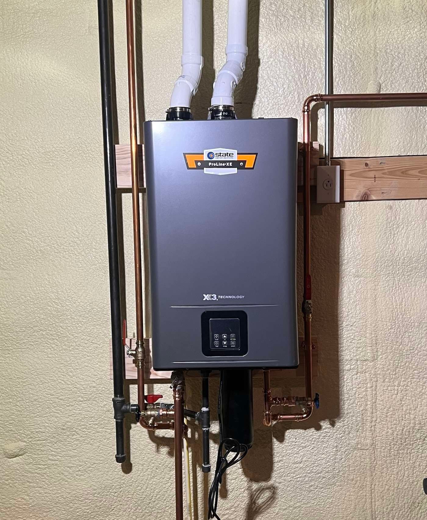 Gray wall-mounted tankless water heater with pipes and ducting in a utility area