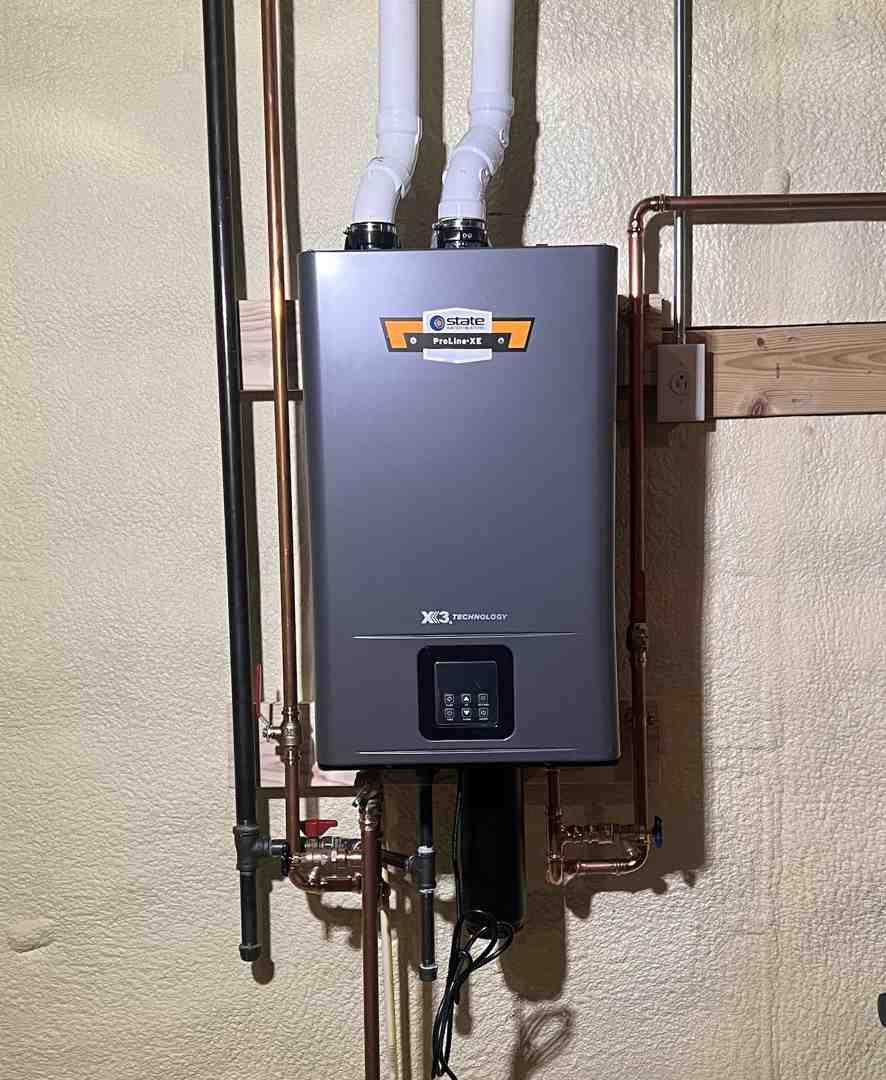 Gray tankless water heater mounted on a wall with white pipes and copper plumbing nearby.