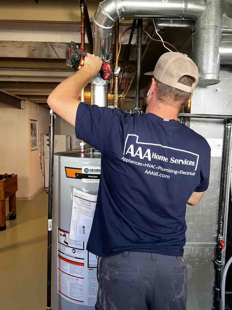 Technician in navy shirt works on home furnace and ductwork in a basement utility area