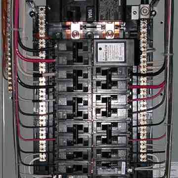 Electrical breaker panel with rows of black circuit breakers and red/black wires inside a metal cabinet