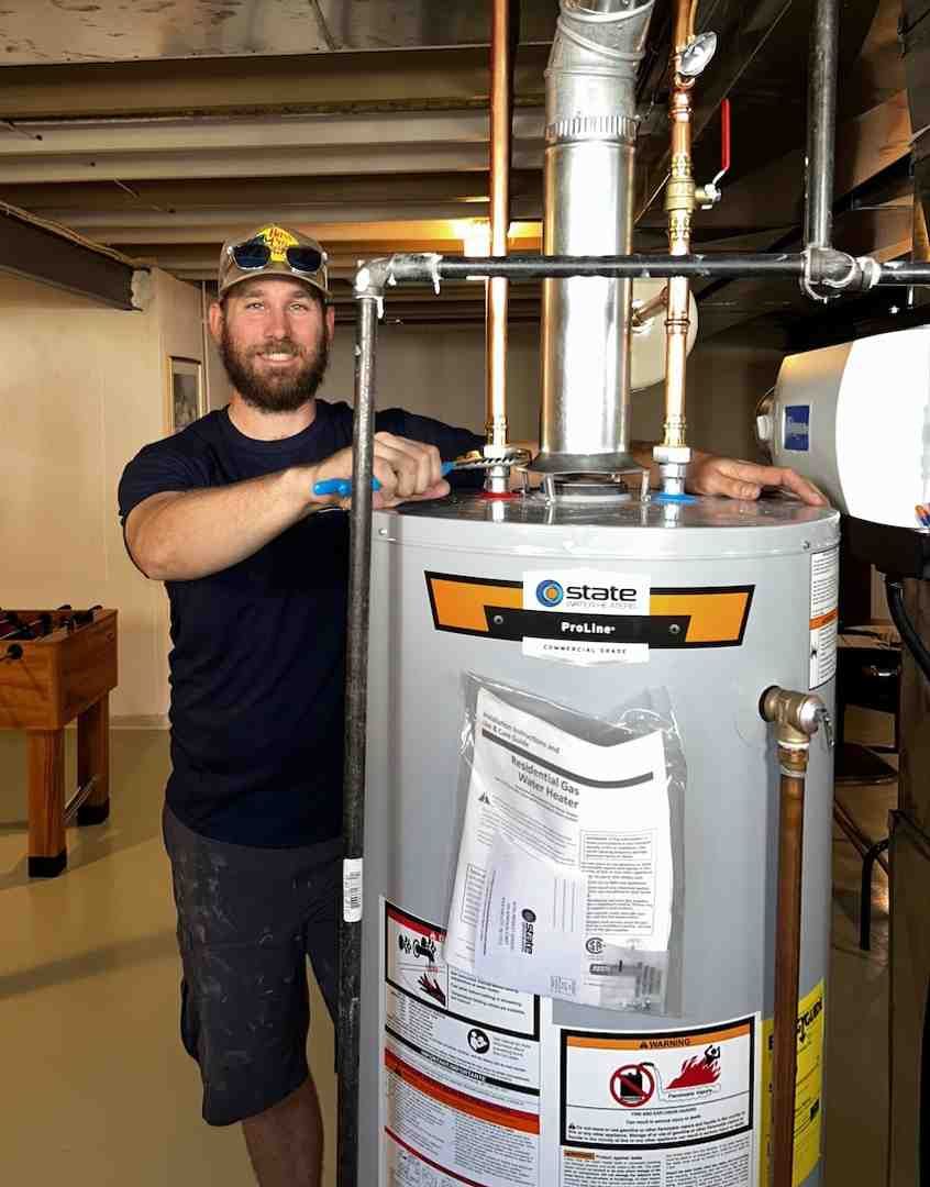 Worker beside a water heater in a basement, adjusting pipes above the tank.