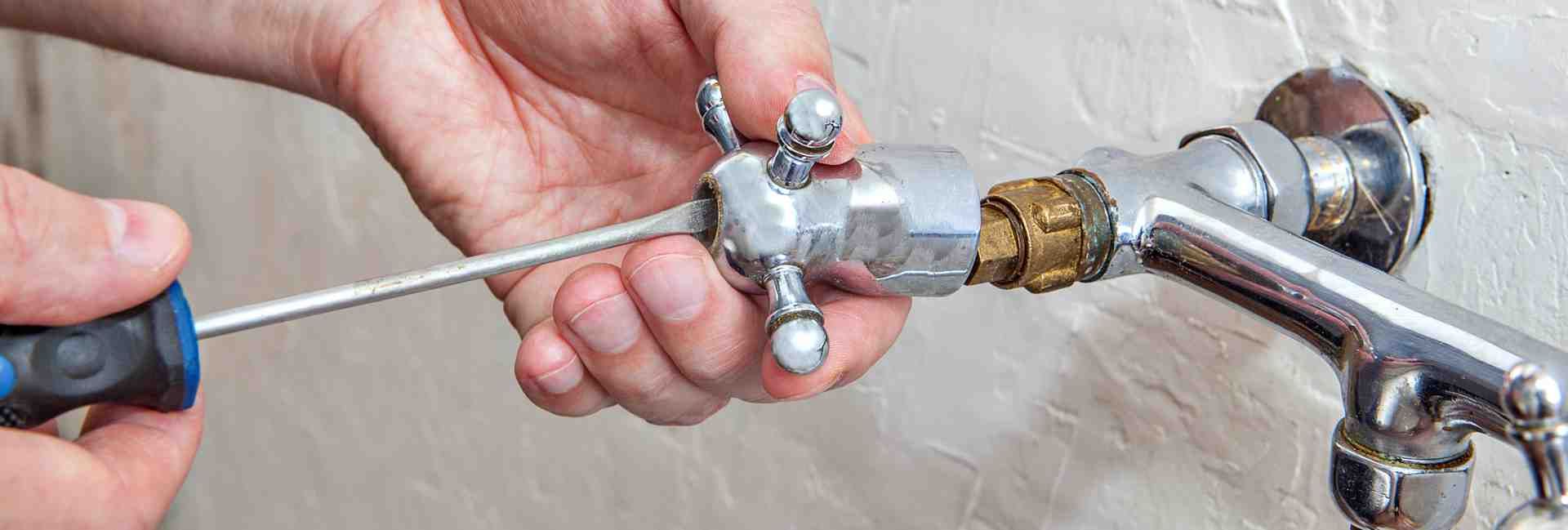 Hands tightening a faucet valve with pliers on a wall-mounted pipe assembly