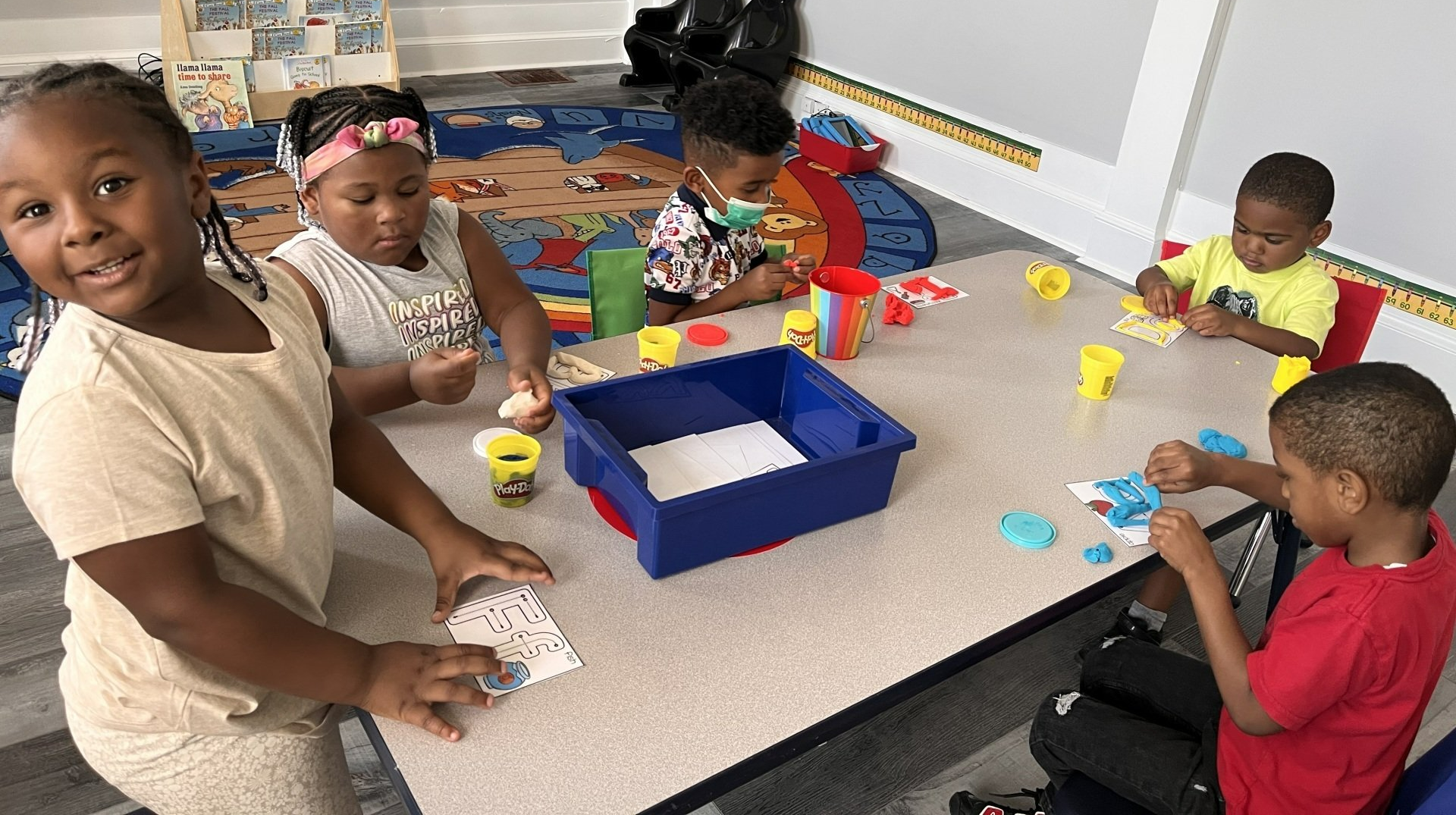 A group of children are sitting at a table playing with play dough.