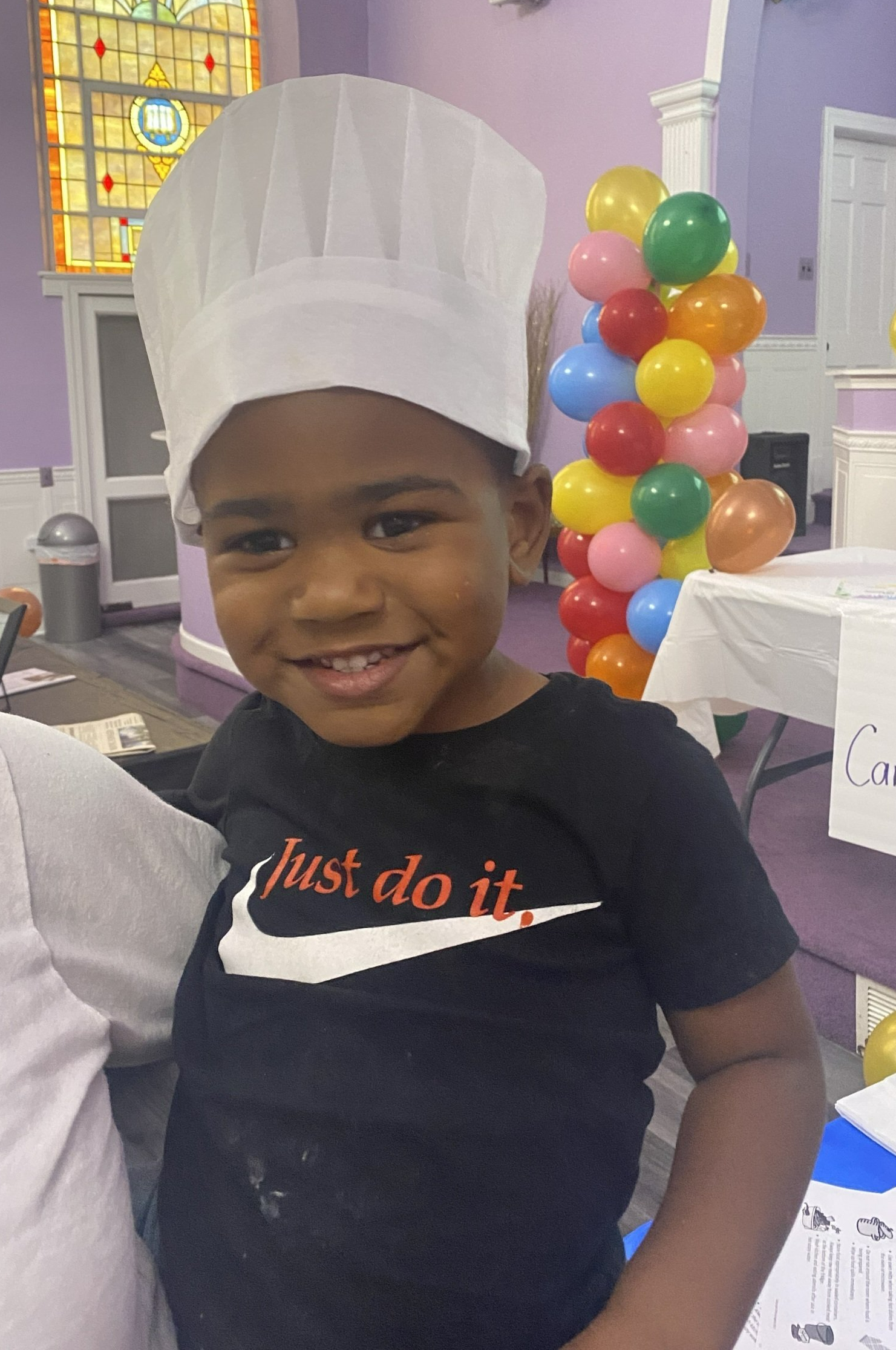 A little boy wearing a chef 's hat and a shirt that says just do it