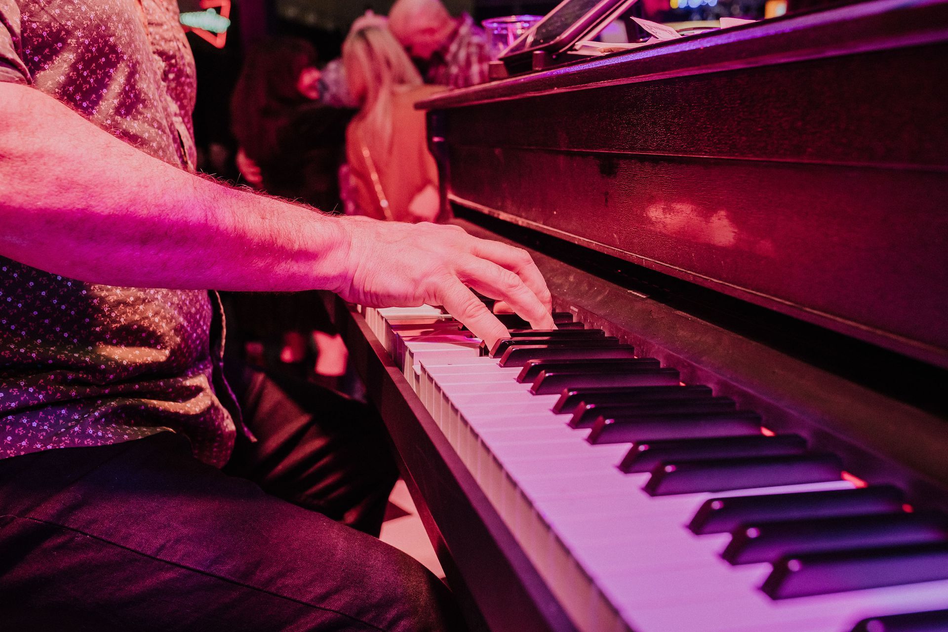 A man is playing a piano with purple lights behind him.