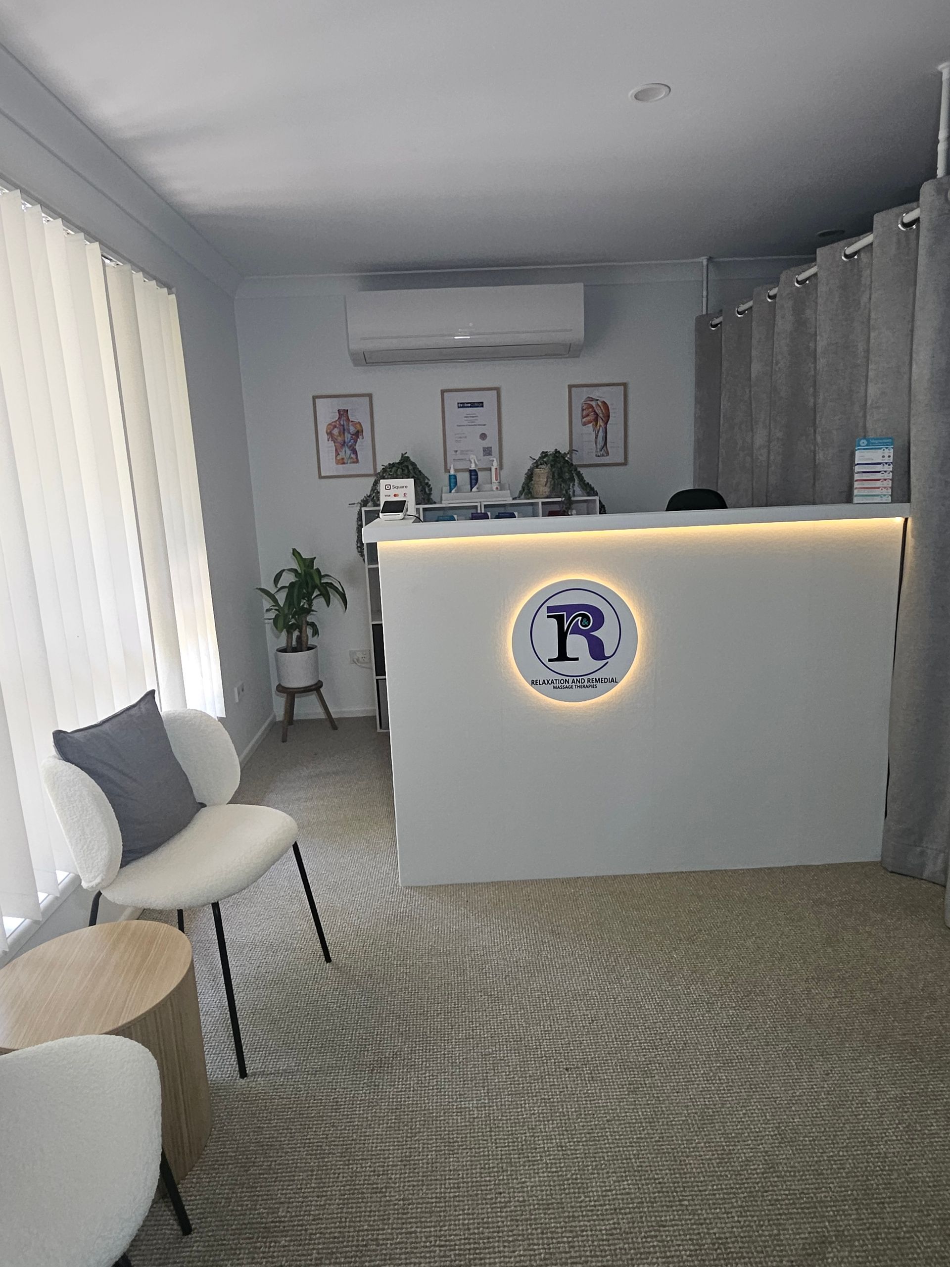 A White Reception Desk in A Clinic, with A Logo and Chair — R & R Relaxation and Remedial In Yamba, NSW
