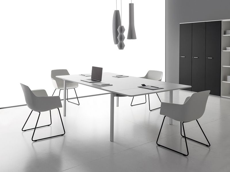 Tavolo da conferenza bianco con sedie, computer portatile e lampade a soffitto in un ufficio moderno.