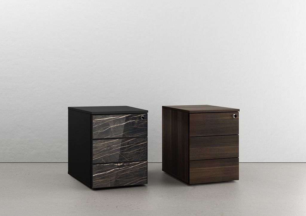 Due piccoli e moderni mobili contenitori a tre cassetti sono posizionati uno accanto all'altro; uno ha una facciata scura con motivo decorativo, l'altro è in legno massello.