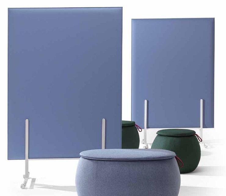 Due divisori in tessuto blu si trovano dietro tre pouf rotondi imbottiti nei toni del blu e del verde scuro.