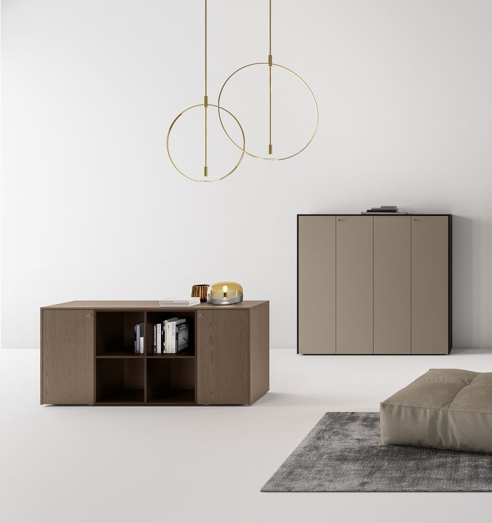 Una stanza minimalista con un mobile contenitore basso in legno, un armadio alto color tortora, due lampade a sospensione circolari e un tappeto grigio.