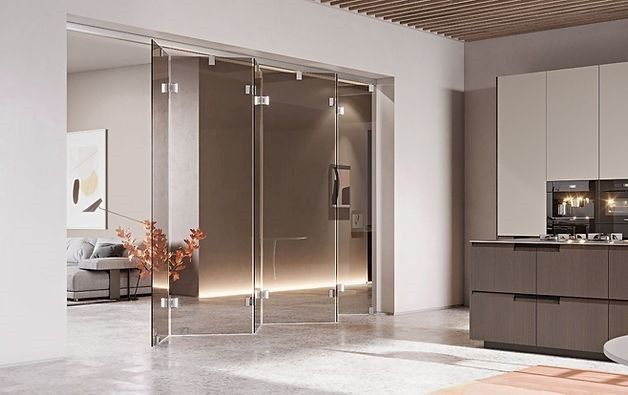 Un interno moderno con una parete divisoria in vetro pieghevole che separa la cucina dalla zona giorno, caratterizzato da un arredamento dai toni neutri.