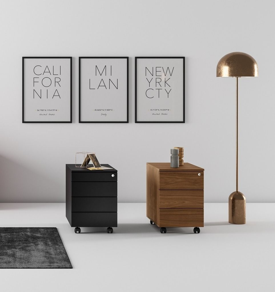 Un mobiletto con cassetti e rotelle, uno nero e uno in legno, è affiancato a tre poster incorniciati e a una lampada da terra dorata.