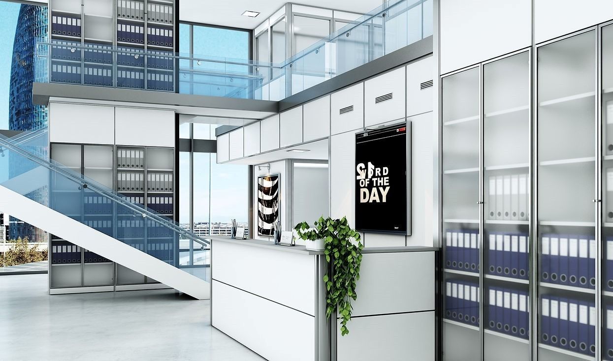 Area reception moderna e minimalista con scrivanie bianche, schedari con ante in vetro, una pianta e un'insegna centrale.