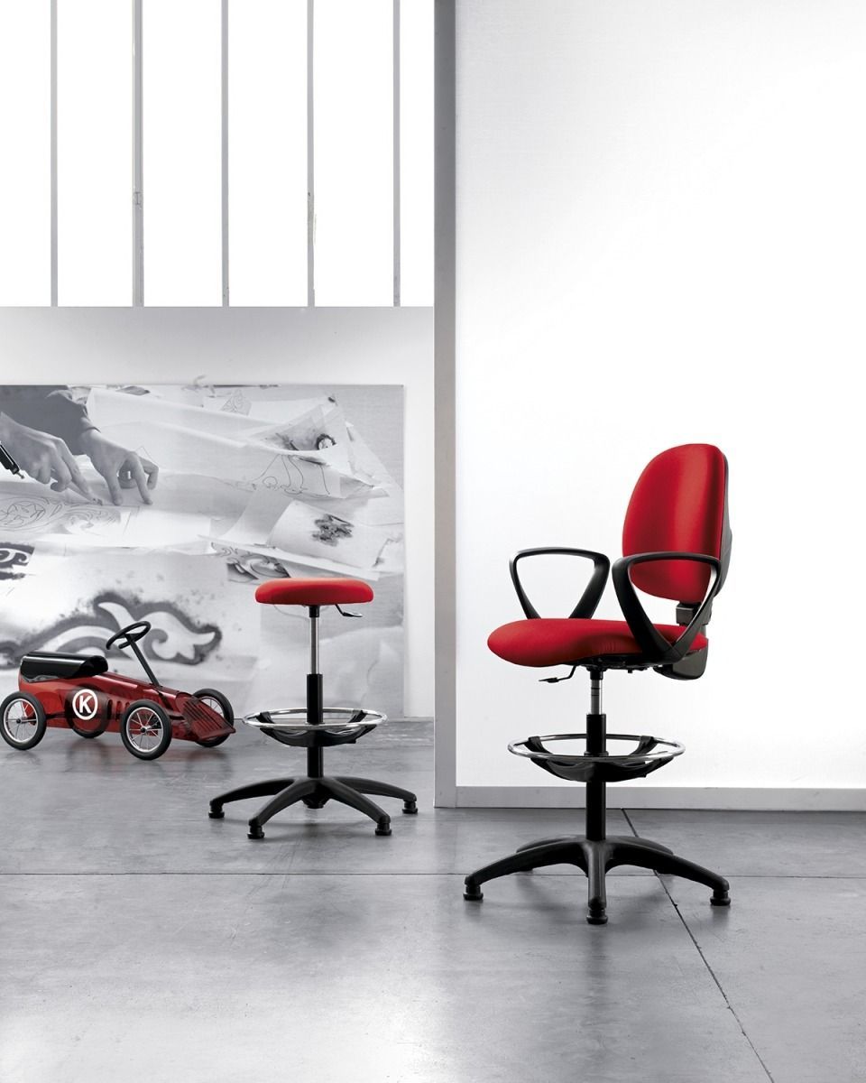 In uno studio minimalista, una sedia da disegno rossa e uno sgabello rosso abbinato sono posizionati su un pavimento grigio.