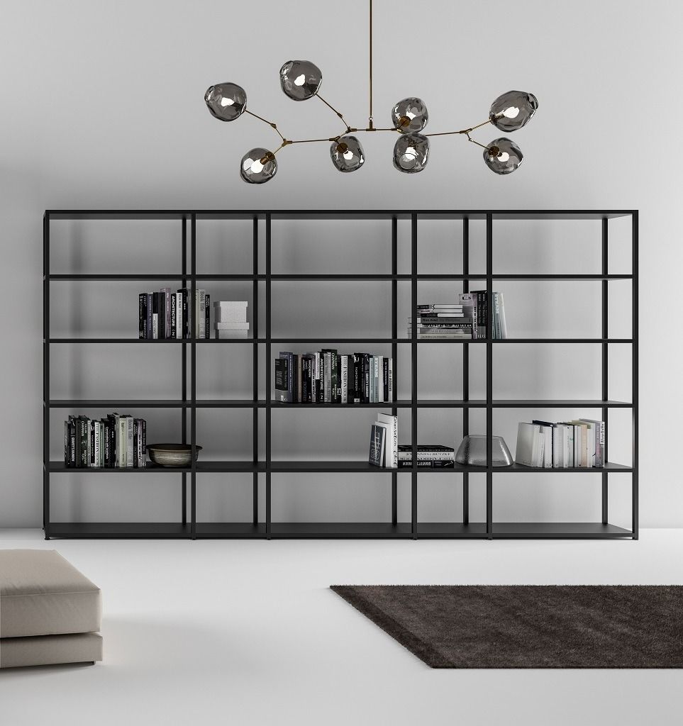 Una moderna libreria in metallo nero con pochi libri, posizionata sotto una lampada a sospensione con paralumi in vetro a più sfere in una stanza minimalista.