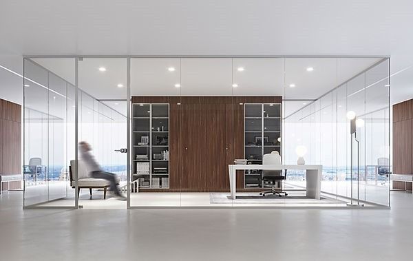 Un moderno ufficio con pareti in vetro e una parete di fondo in legno, arredato con una scrivania, scaffali e una persona seduta su una sedia.