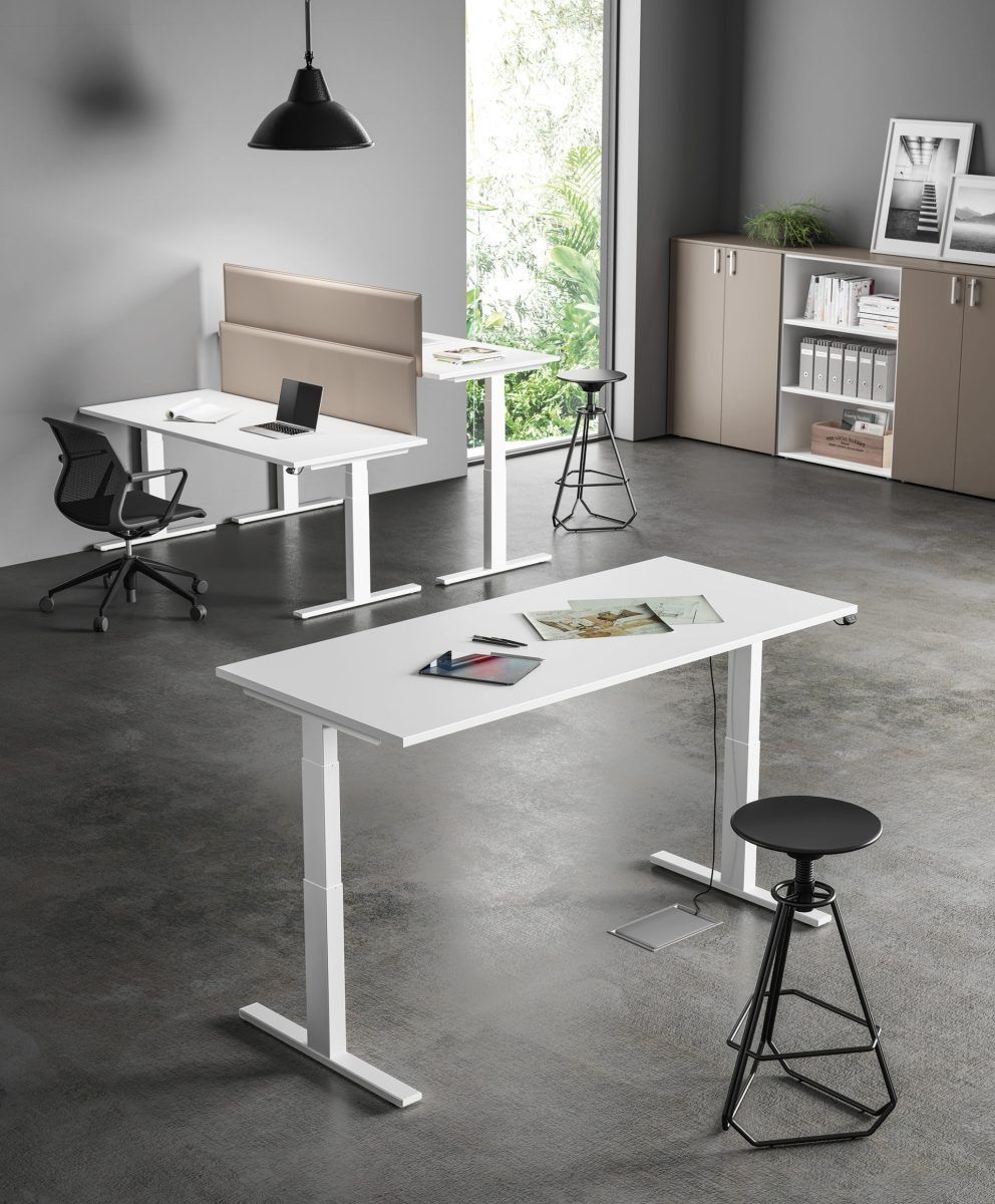 Due scrivanie regolabili in altezza di colore bianco, complete di sedia e sgabelli, in un ufficio moderno e minimalista con pareti grigie.
