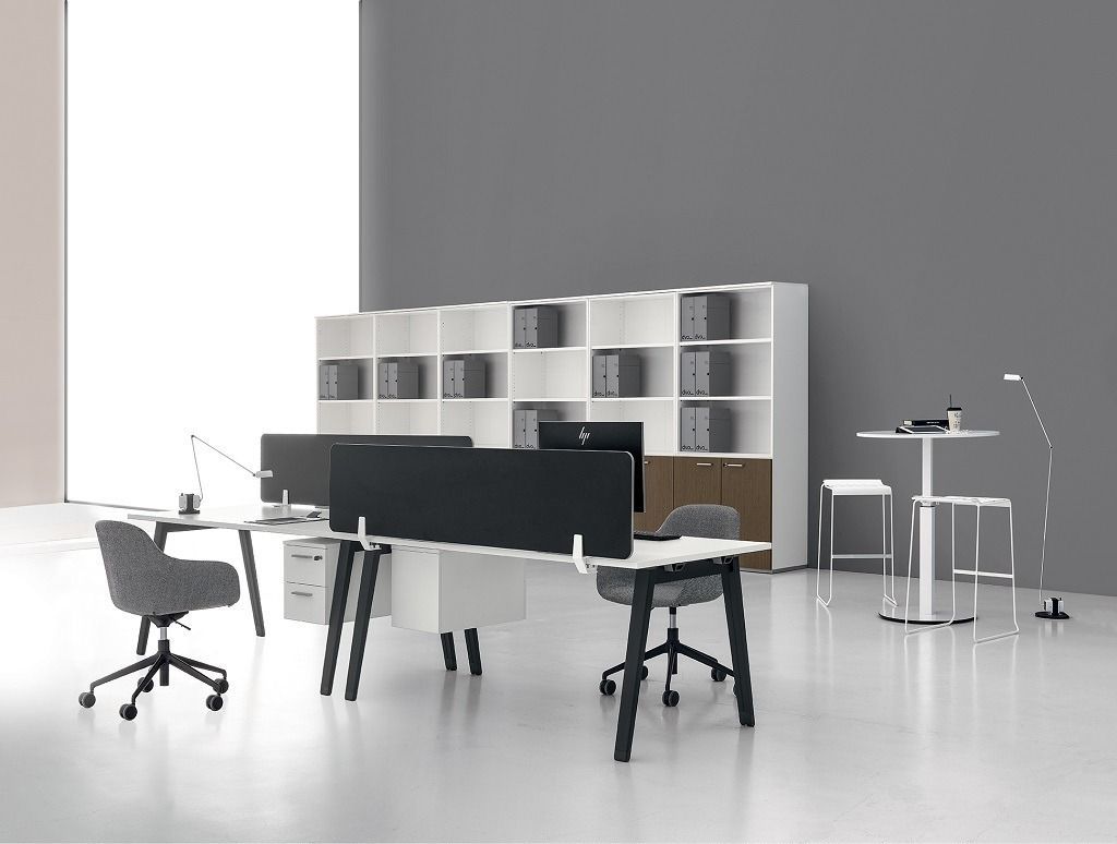 Un moderno interno d'ufficio caratterizzato da postazioni di lavoro con schermi divisori neri, sedie ergonomiche e scaffalature bianche.