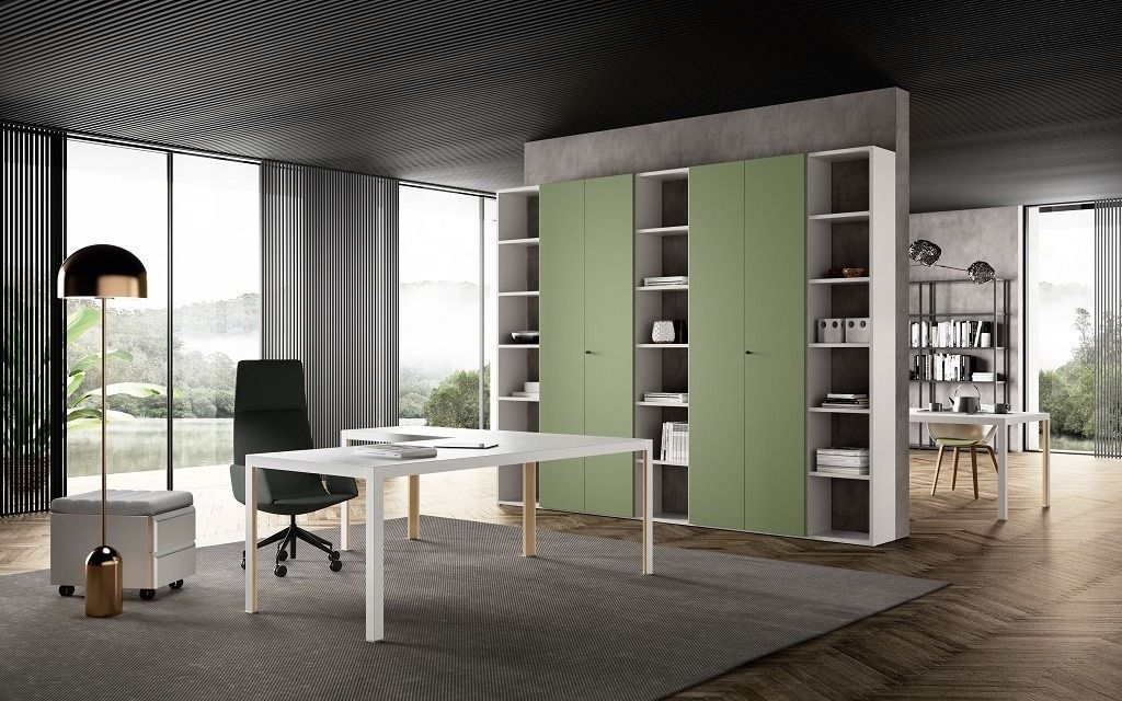 Un moderno ufficio domestico con scrivania bianca, sedia nera e mobile contenitore verde salvia con ripiani a vista su un tappeto grigio.