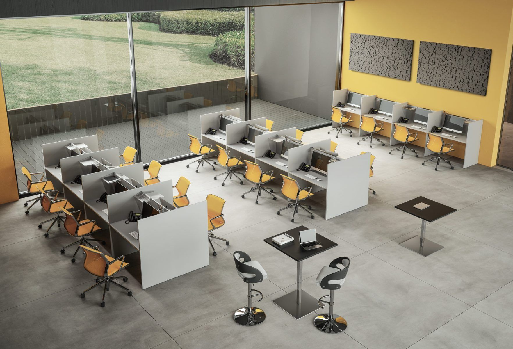 Un ufficio con file di cubicoli, sedie gialle, due tavoli alti e una grande finestra che si affaccia su un prato.