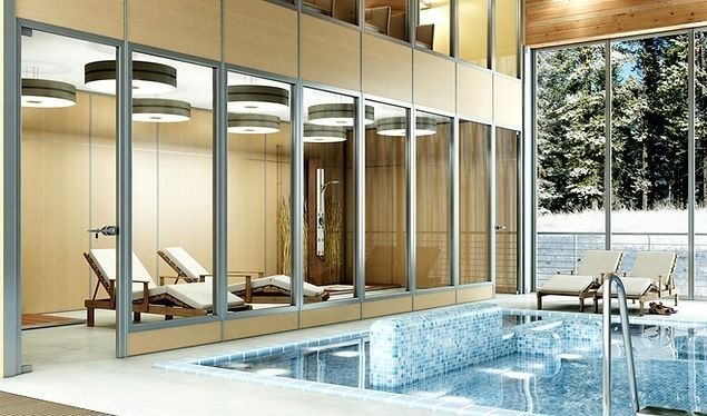 Piscina coperta e area benessere con lettini prendisole visibili attraverso pannelli di vetro e vista su una foresta innevata.