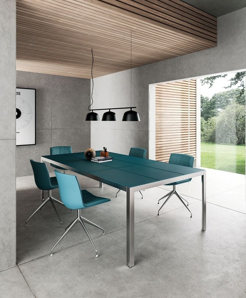 Una sala da pranzo moderna con un lungo tavolo color verde acqua e sedie girevoli abbinate, illuminate da un lampadario a sospensione a tre luci.