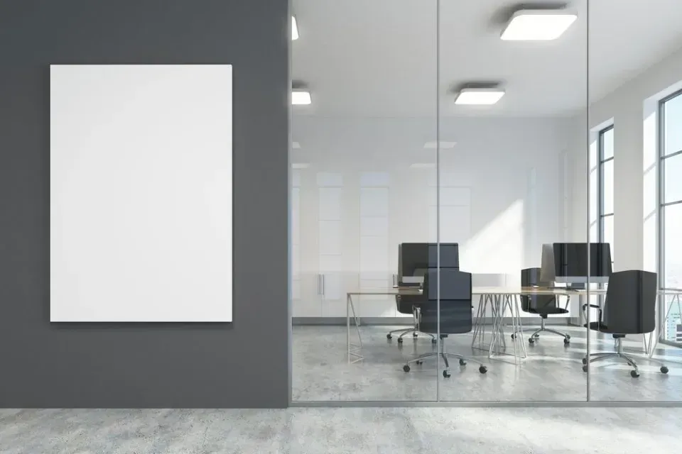 Un cartello rettangolare bianco è appeso a una parete grigio scuro accanto a una moderna sala conferenze con pareti in vetro.