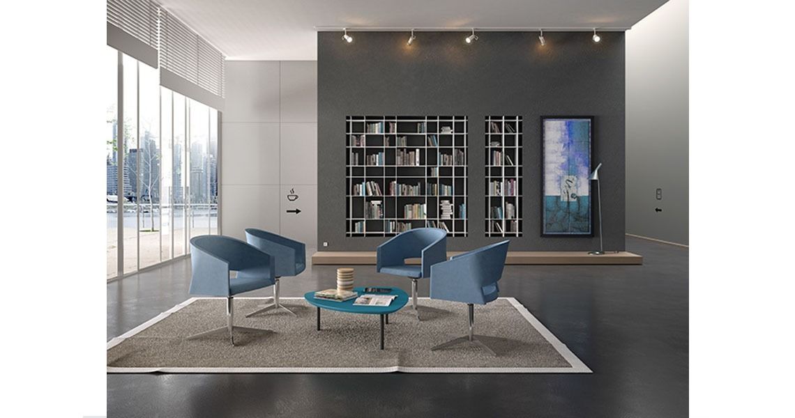 In un moderno ufficio con librerie, quattro poltrone blu sono disposte attorno a un tavolino color verde acqua su un tappeto grigio.