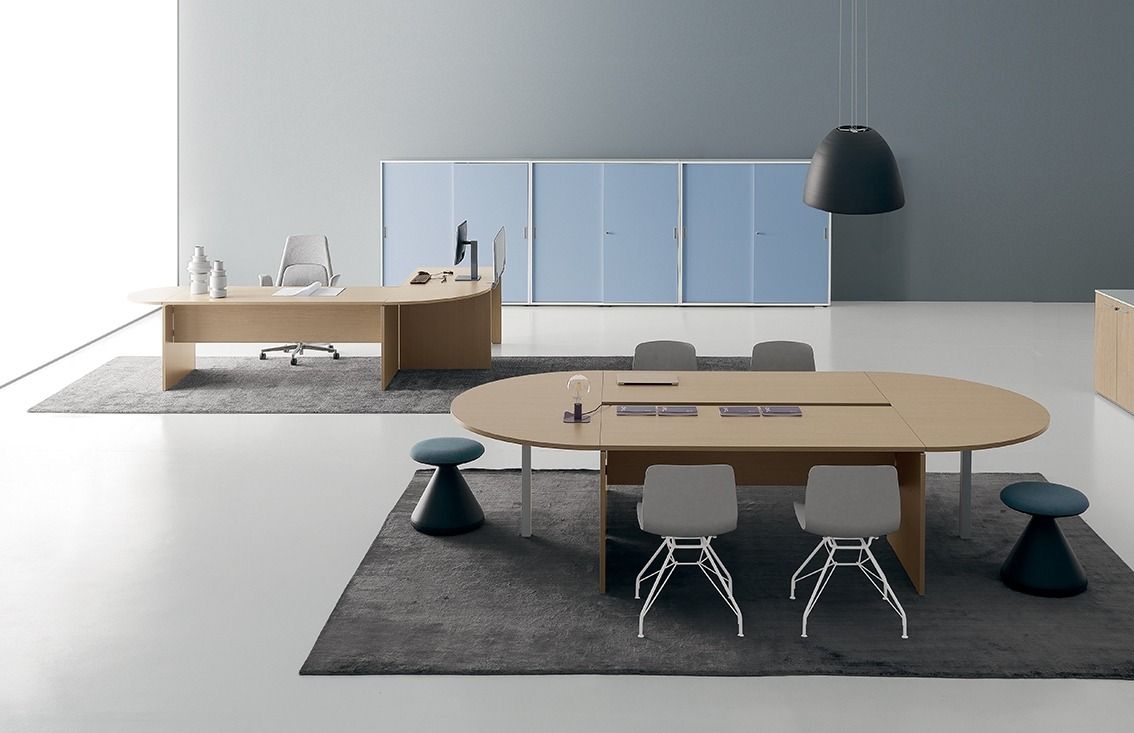 Ufficio moderno con scrivania in legno chiaro, tavolo da conferenza ovale con sgabelli e sedie e armadietti azzurri.