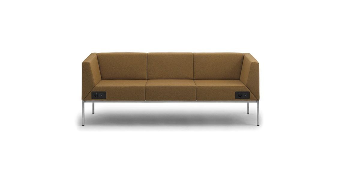 Un divano moderno a tre posti color beige con gambe in metallo argentato e prese di corrente nere integrate nella struttura frontale.