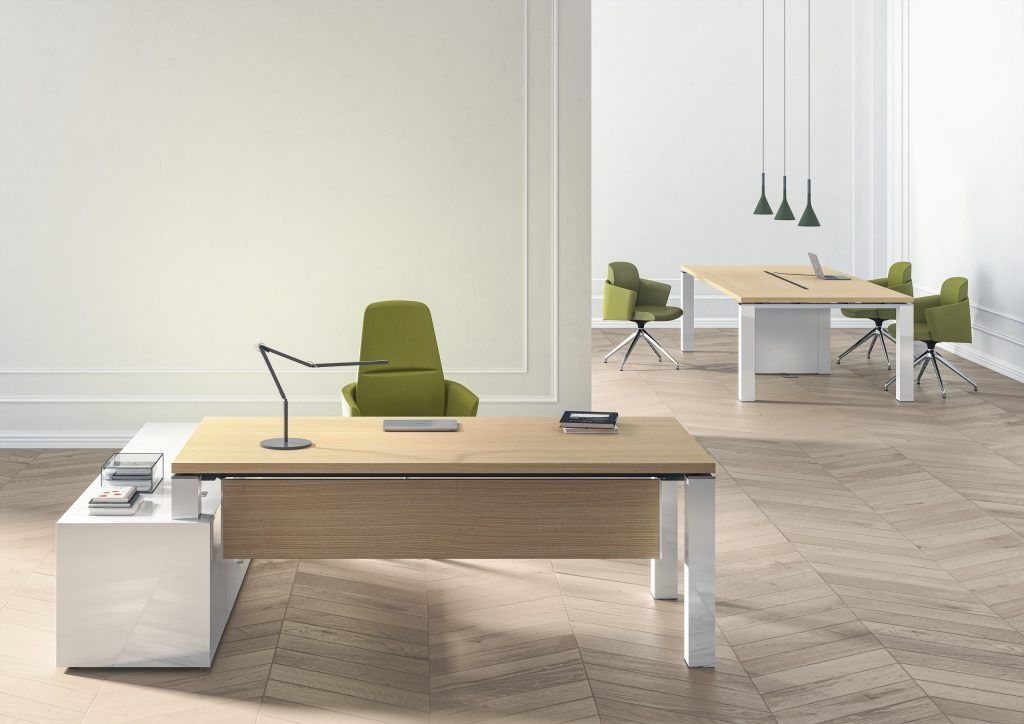 Un ufficio moderno con due scrivanie in legno chiaro, gambe bianche e sedie verde oliva, su uno sfondo di pareti bianche e pavimento in legno.