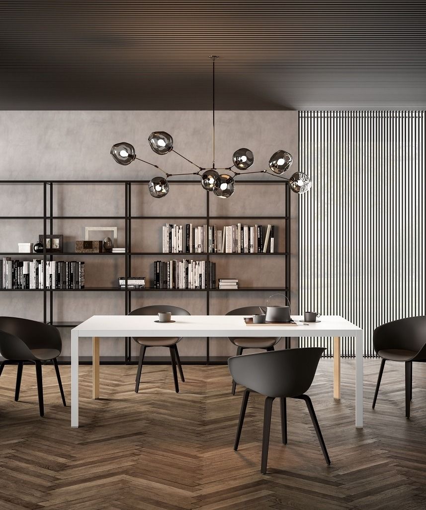 Un moderno set da pranzo con tavolo bianco e quattro sedie grigio scuro, inserito in una stanza con libreria e lampadario in metallo nero.