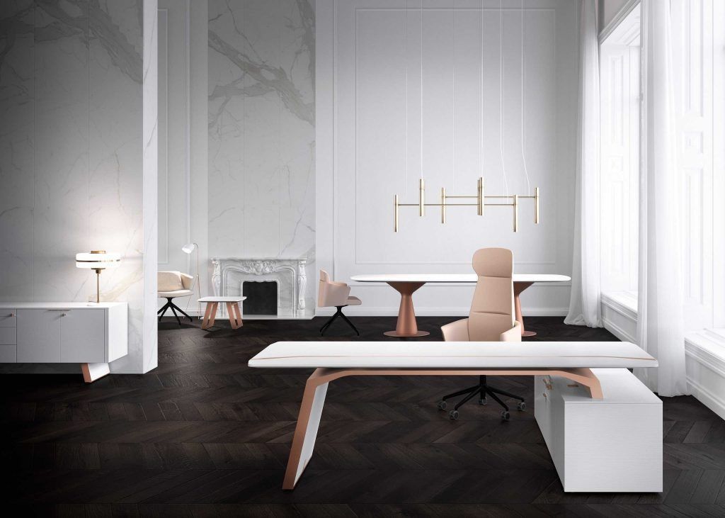 Ufficio moderno con scrivanie bianche minimaliste, dettagli color oro rosa, sedie e un camino addossato a una parete di marmo.